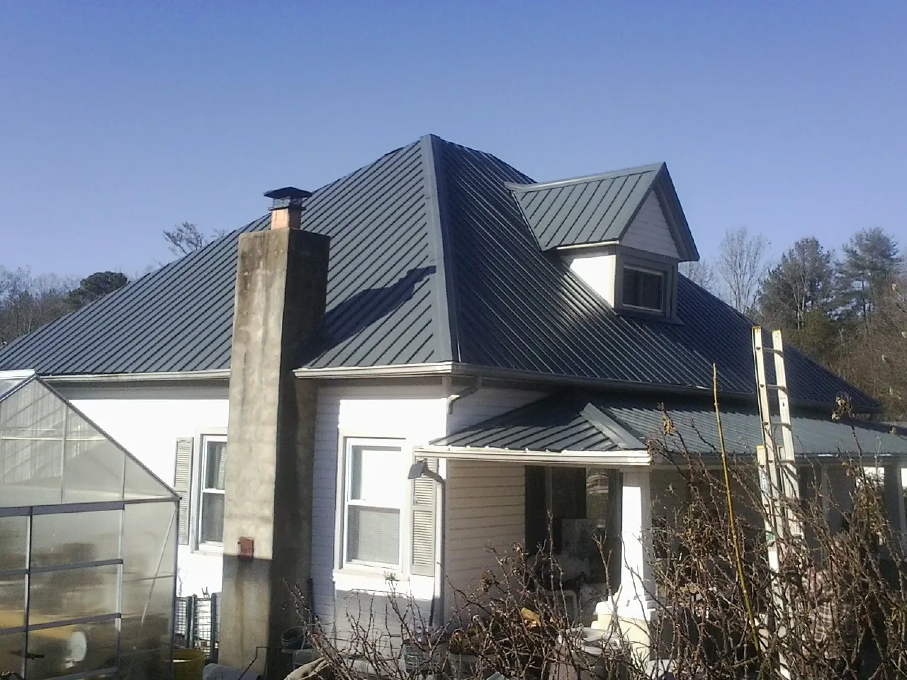Dark blue standing seam metal roof on a white farmhouse with dormer in Eutaw