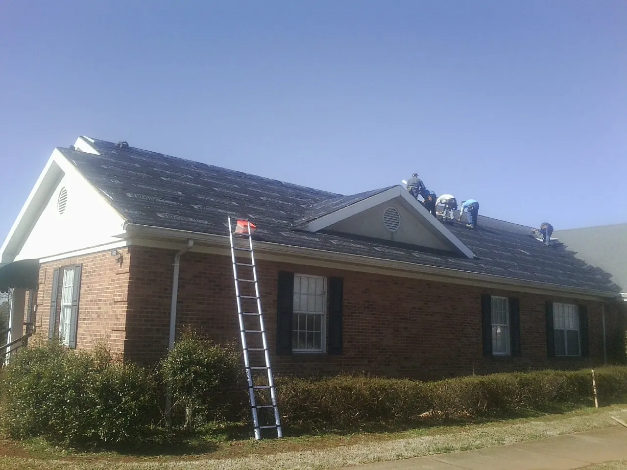 Crew tearing shingles off a brick ranch roof with a ladder set — Metal Roof Repair work by our crew in Eutaw