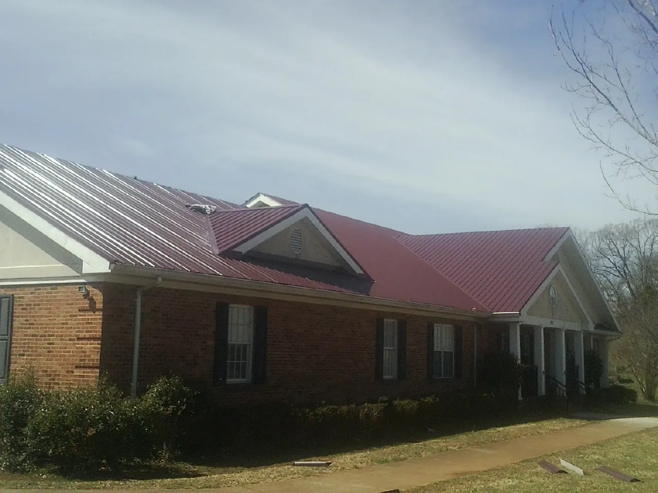Red metal roof with gabled entries on a long brick building, from a Hail Damage Roof Repair job in Eutaw