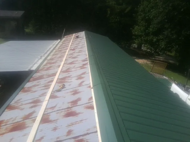 Old rusted panels beside newly installed green metal roofing — Wind Damage Roof Repair by Roofing Brothers in Eutaw