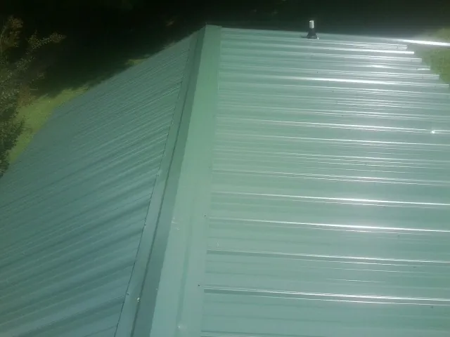 New green metal panels meeting at the ridge of a roof — Flat Roof Repair work by our crew in Eutaw