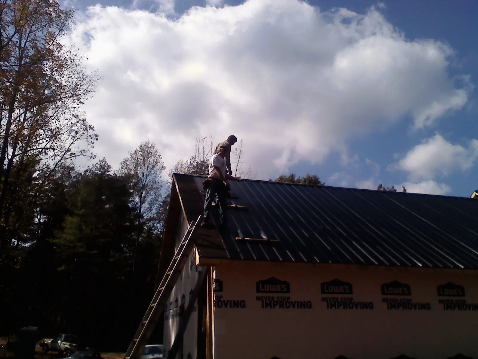 Roofer fastening dark metal panels high against a cloudy sky, from a Roof Inspection job in Eutaw