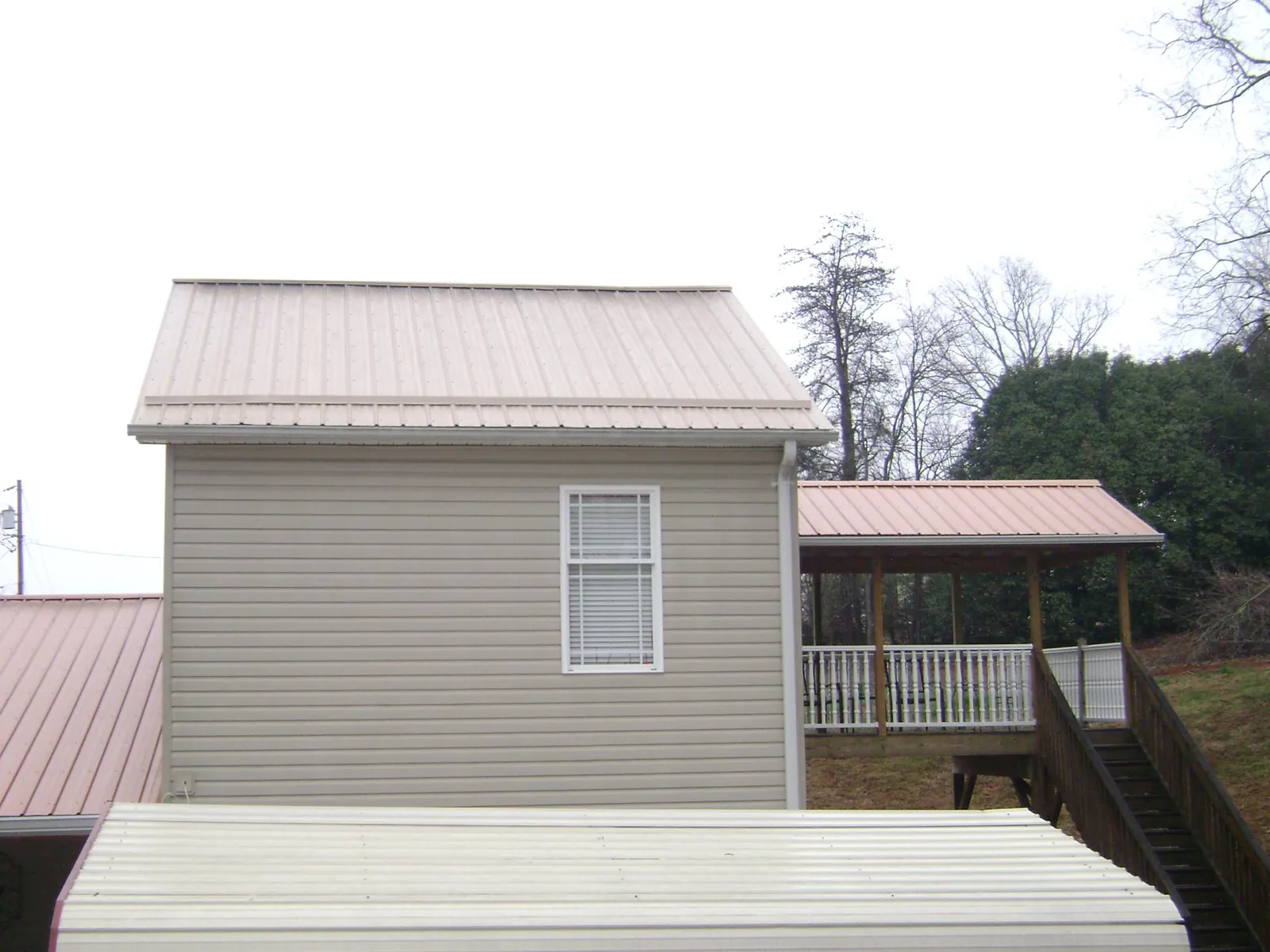 Tan metal roofs on a two story addition and attached porch, from a Roof Replacement job in Eutaw
